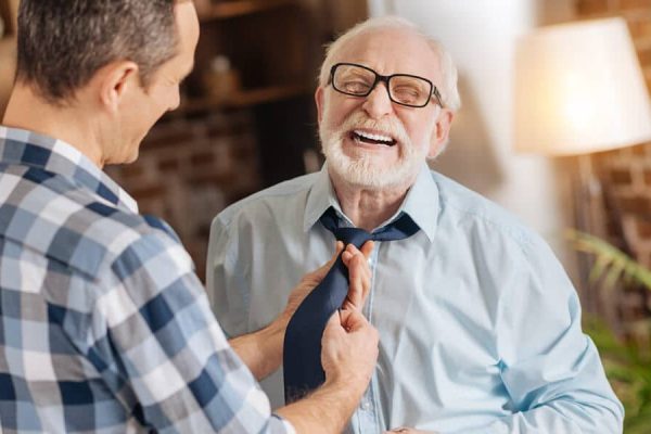 In-home caregiver tying tie for senior